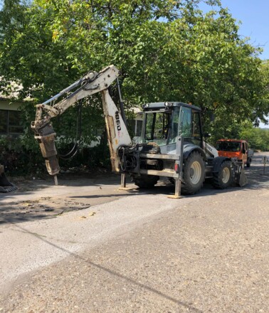 Backhoe loader with hydraulic breaker performing roadwork, depicting construction activity on a linear asset for AP Sensing monitoring Backhoe loader with hydraulic breaker performing roadwork, depicting construction activity on a linear asset for AP Sensing monitoring